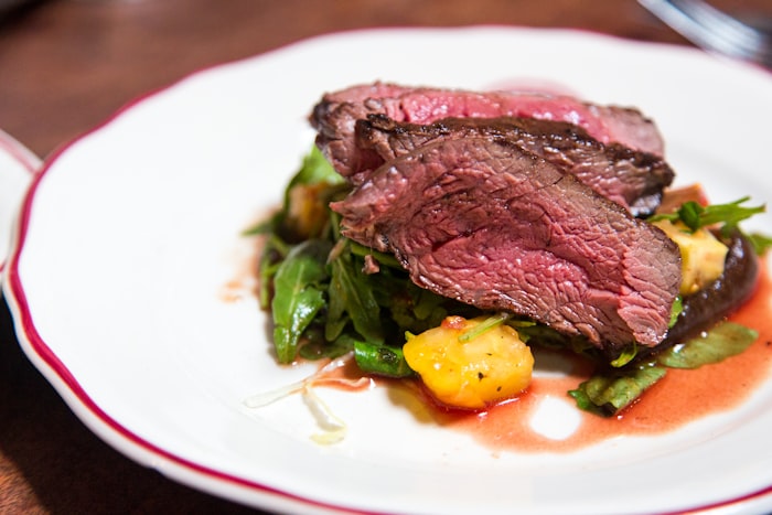 Beautifully plated cooked lamb on a white bistro plate with greens and jus